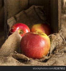 Red apples in rustic setting with old wooden box and hessian sack