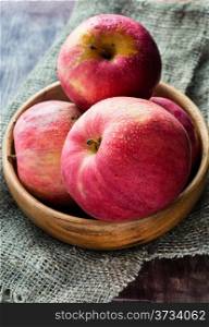 Red apples in wooden bowl over rustic background, selective focus