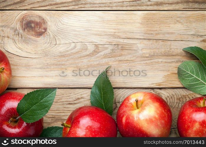 Red apples with green leaves on wooden table. Top view
