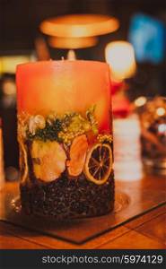 Red aromatic candle with coffee beans and orange slices on a glass stand. Handmade aromatic candle