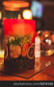 Red aromatic candle with coffee beans and orange slices on a glass stand. Handmade winter bar