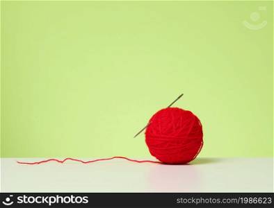 red ball with woolen thread on white table, green background