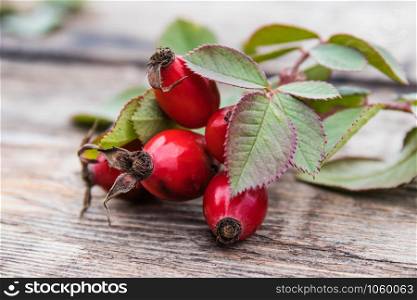 Red berries and rosehip leaves on a wooden table. Close-up.. Red berries and rosehip leaves on a wooden table. C