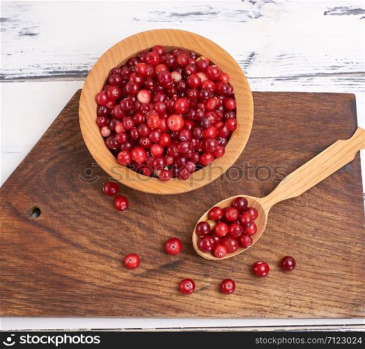 red berries of ripe lingonberries in a wooden bowl on a table, top view