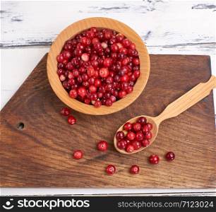 red berries of ripe lingonberries in a wooden bowl on a table, top view
