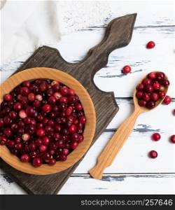 red berries of ripe lingonberries in a wooden bowl on a white table, top view