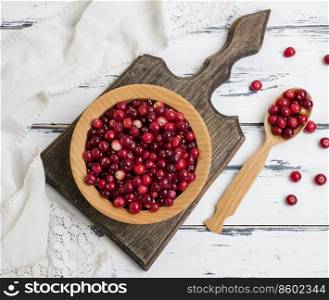 red berries of ripe lingonberries in a wooden bowl on a white table, top view