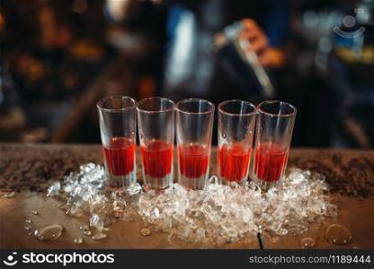 Red beverages in a glasses and ice on bar counter closeup, nobody. Refreshing of alcoholic drink, cold crystals on the table. Red beverages in a glasses and ice on bar counter