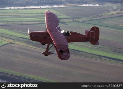 Red Bi-wing Plane Flying Over Fields