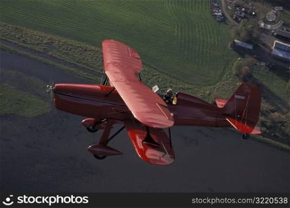 Red Bi-wing Plane Flying Over Water And Farms