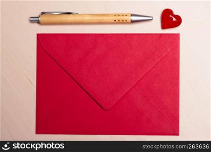 Red blank envelope little heart and pen on wooden surface. Valentine day card, love or wedding greeting concept.