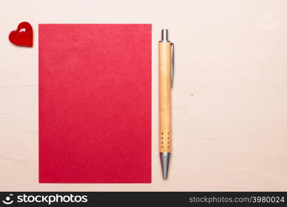 Red blank sheet of paper with heart love symbol and pen on wooden surface. Background for valentines day or wedding card.