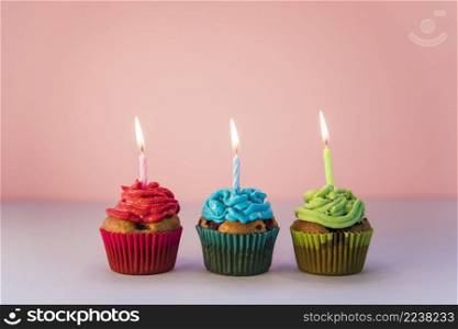red blue green cupcakes with lighted candles against pink backdrop