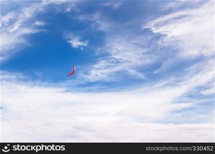 Red boomerang flies in the blue sky among pure white clouds.. Red boomerang in flight