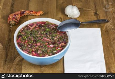 Red borscht in a blue porcelain bowl stands on a wooden table
