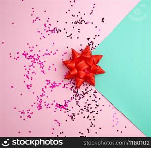 red bow and shiny multicolored round confetti scattered on a pink-green abstract background, festive backdrop for birthday, valentines day