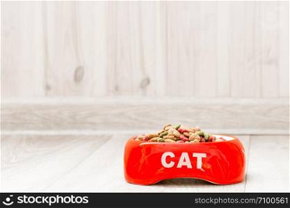 Red bowl for a cat with dry food on the floor in the house close-up