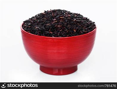 Red bowl of raw organic black venus rice on white background.