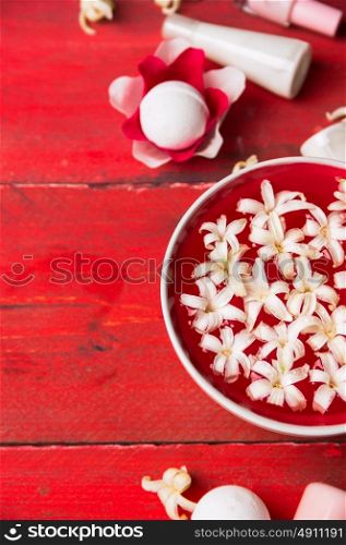 Red bowl with white flowers in water, bottle with lotion on wooden table , spa background, top view