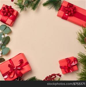 Red boxes with gifts, fir branches with Christmas decor on a beige background, erhu view. Copy space