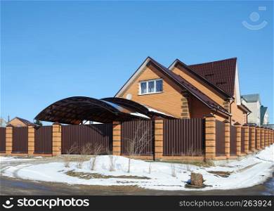 Red brick cottage witn garage behind the metal fence in small russian town, spring time
