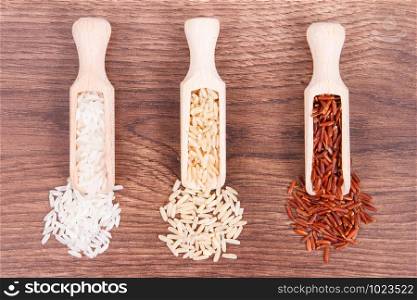 Red, brown and white rice with wooden scoop on rustic board, concept of healthy nutrition. Red, brown and white rice with wooden scoop on rustic board, healthy food