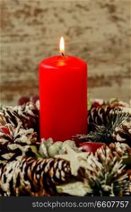 Red candle lit and pinecones for Christmas on a wooden background
