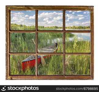 red canoe on lake shore in summer scenery as seen through vintage, grunge, sash window with dirty glass