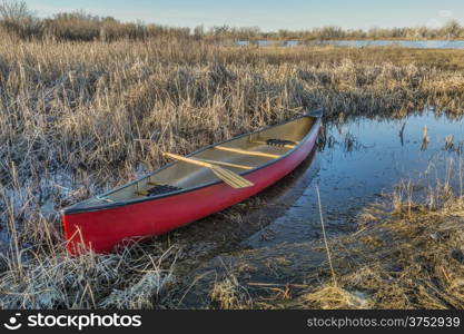red canoe with a wooden paddle in a wetland, early spring