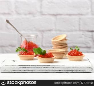 red caviar in a glass jar and round tartlets on a white table, close up
