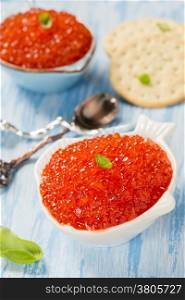 Red caviar in fish-shape bowl with crackers, closeup, selective focus