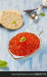 Red caviar in fish-shape bowl with crackers, closeup, selective focus