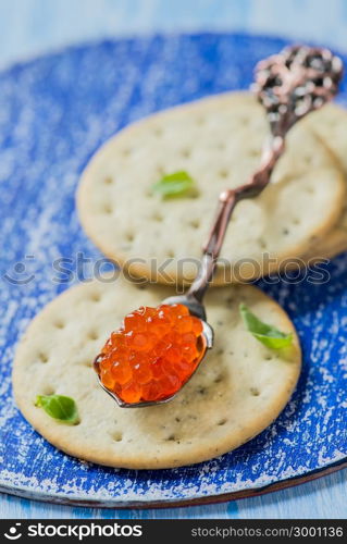 Red caviar in spoon on crackers, closeup