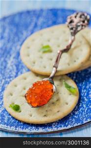 Red caviar in spoon on crackers, closeup