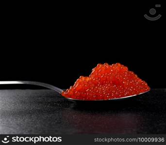 red caviar of chum salmon in a metal spoon on a black background, close up