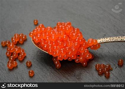 red caviar of chum salmon in a metal spoon on a black background, close up