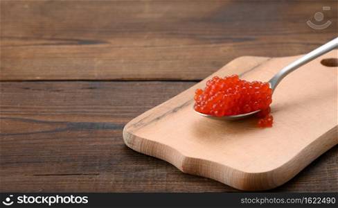 red caviar of pink salmon lies in a wooden spoon. Brown wooden table