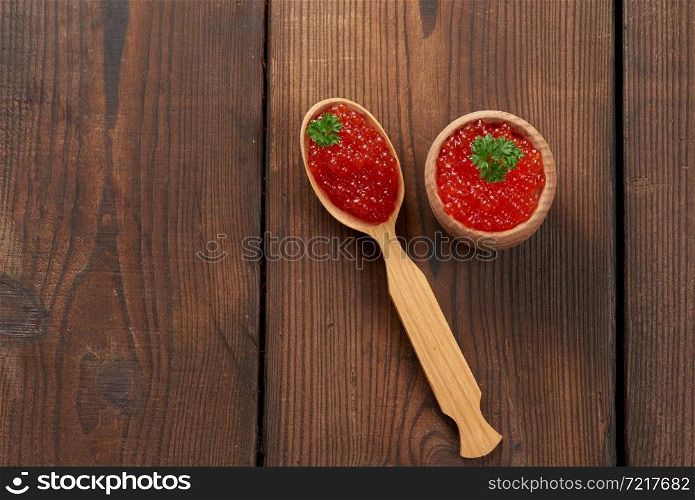 red caviar of pink salmon lies in a wooden spoon. Brown wooden table, top view