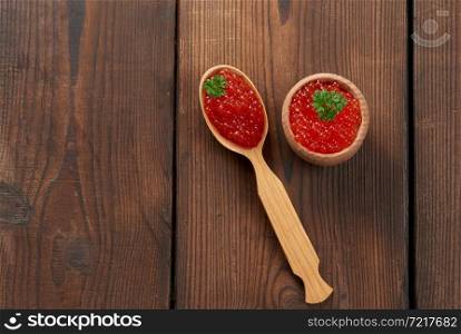 red caviar of pink salmon lies in a wooden spoon. Brown wooden table, top view