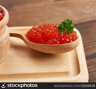 red caviar of pink salmon lies in a wooden spoon on a brown wooden table, close up