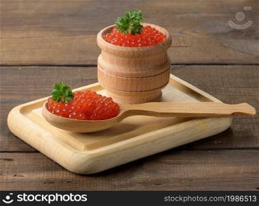 red caviar of pink salmon lies in a wooden spoon on a cutting board. Brown wooden table