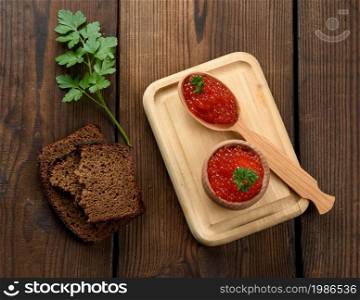 red caviar of pink salmon lies in a wooden spoon on a cutting board. Brown wooden table, top view