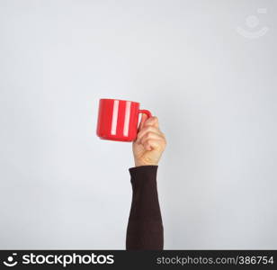 red ceramic cup in a female hand on a white background, hand is raised up