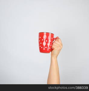 red ceramic cup in a female hand on a white background, the hand is raised up