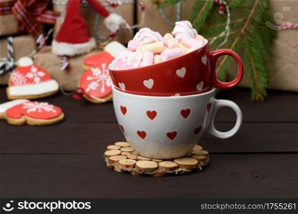 red ceramic cup with cocoa and marshmallows, behind a gift box and a Christmas garland, close up