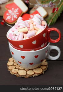 red ceramic cup with cocoa and marshmallows, behind a gift box and a Christmas toy, close up
