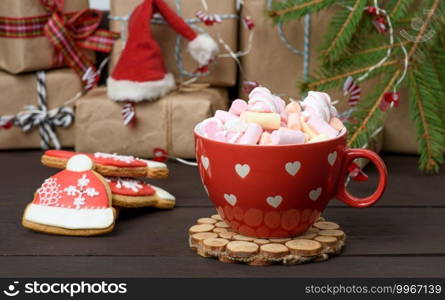 red ceramic cup with cocoa and marshmallows, behind a gift box and a Christmas toy