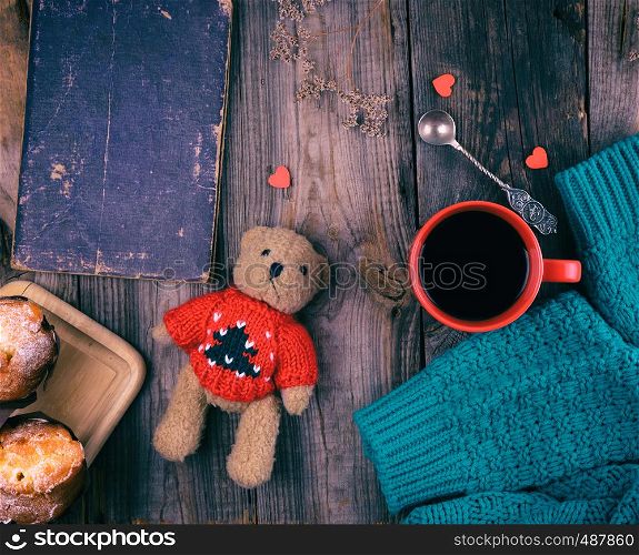 red ceramic mug with black coffee and baked muffins on a wooden board, gray table, top view