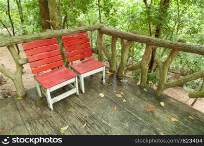 Red chair. Two are located on the wooden deck. Under the trees in the garden.