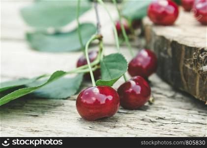 Red cherries and branches with green leaves on a wooden table. Close-up.. Red cherries and branches with green leaves on a wooden table.